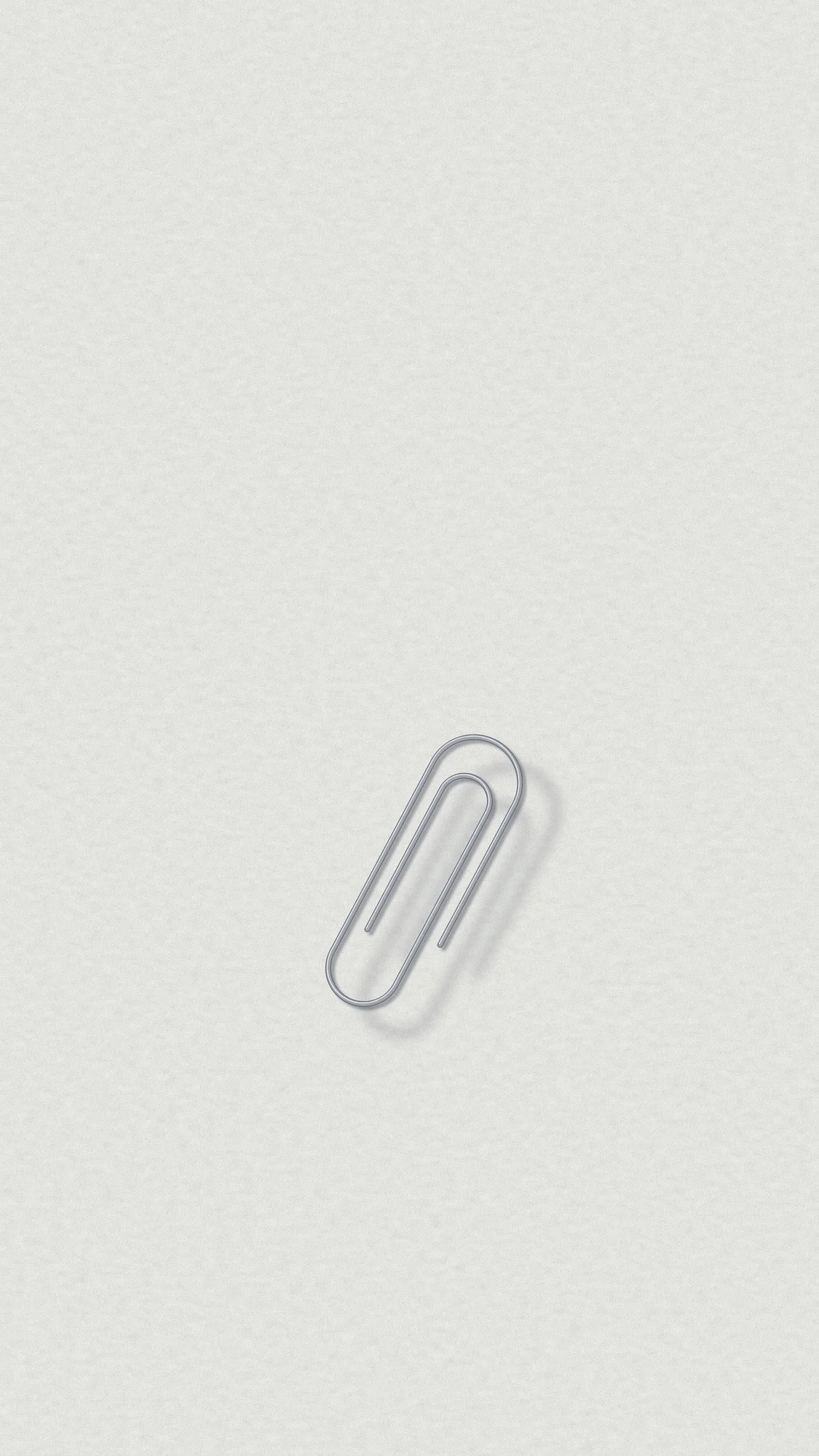 Paperclip: One paperclip and its long soft shadow on a white sheet, placed low and turned steeply across the phone screen.